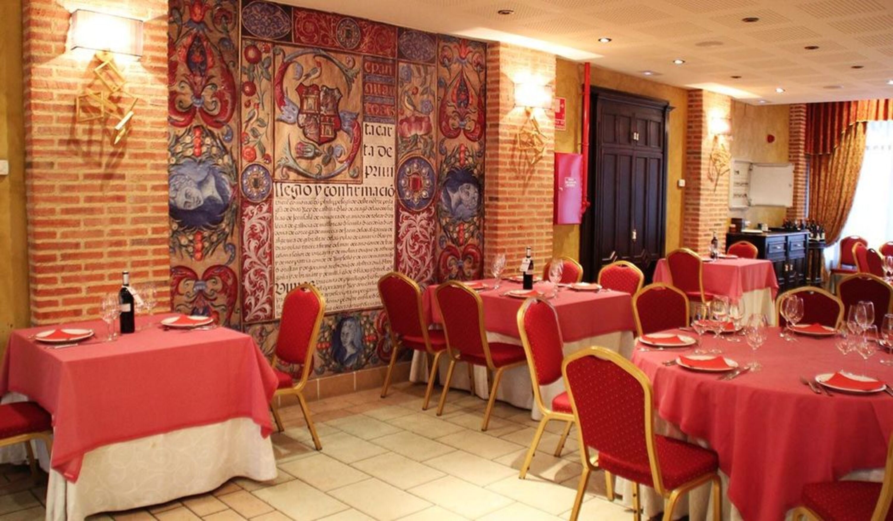 Un comedor con manteles rojos, sillas doradas y una gran pared decorativa con diseños intrincados.