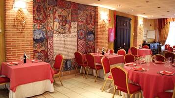 Un comedor con manteles rojos, sillas doradas y una gran pared decorativa con diseños intrincados.