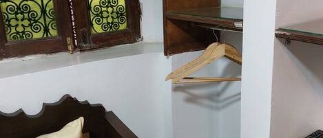 A bedroom with a wooden bed, a window with decorative glass panes, and a small shelf with a remote control.