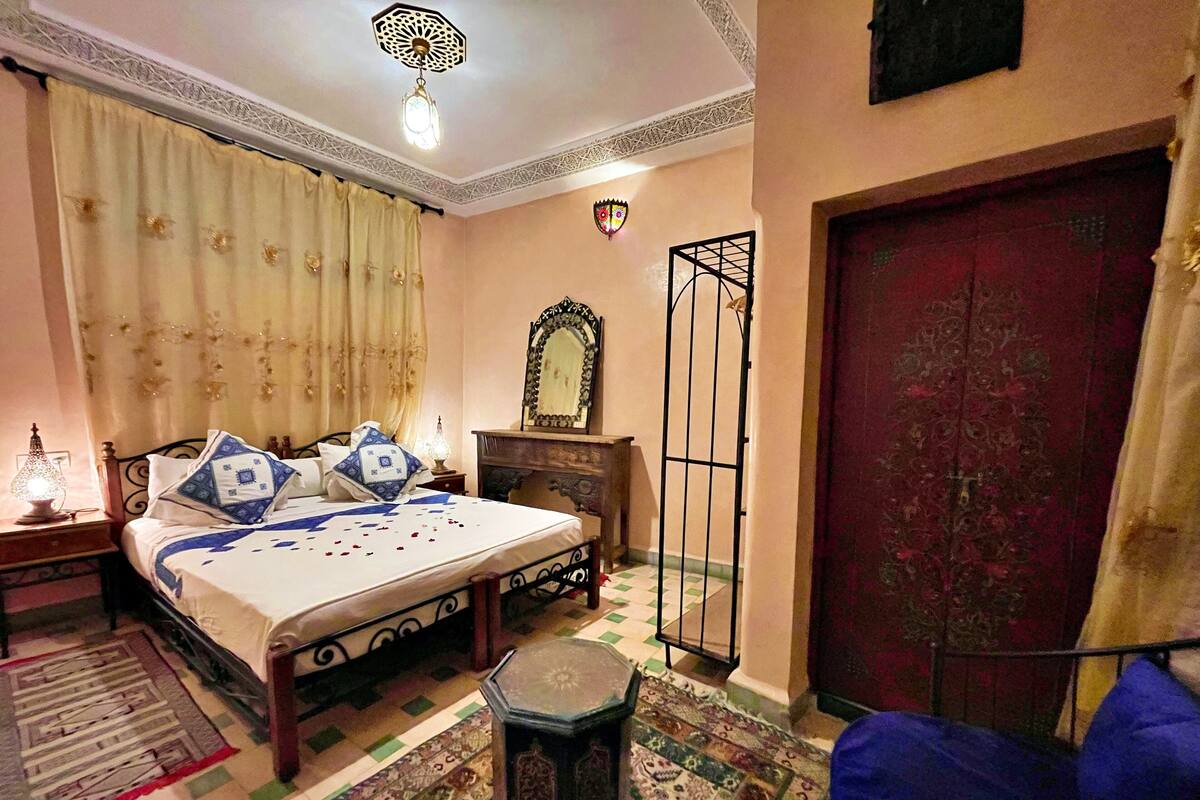 A bedroom with a bed, a nightstand, a mirror, a door, and a patterned rug.