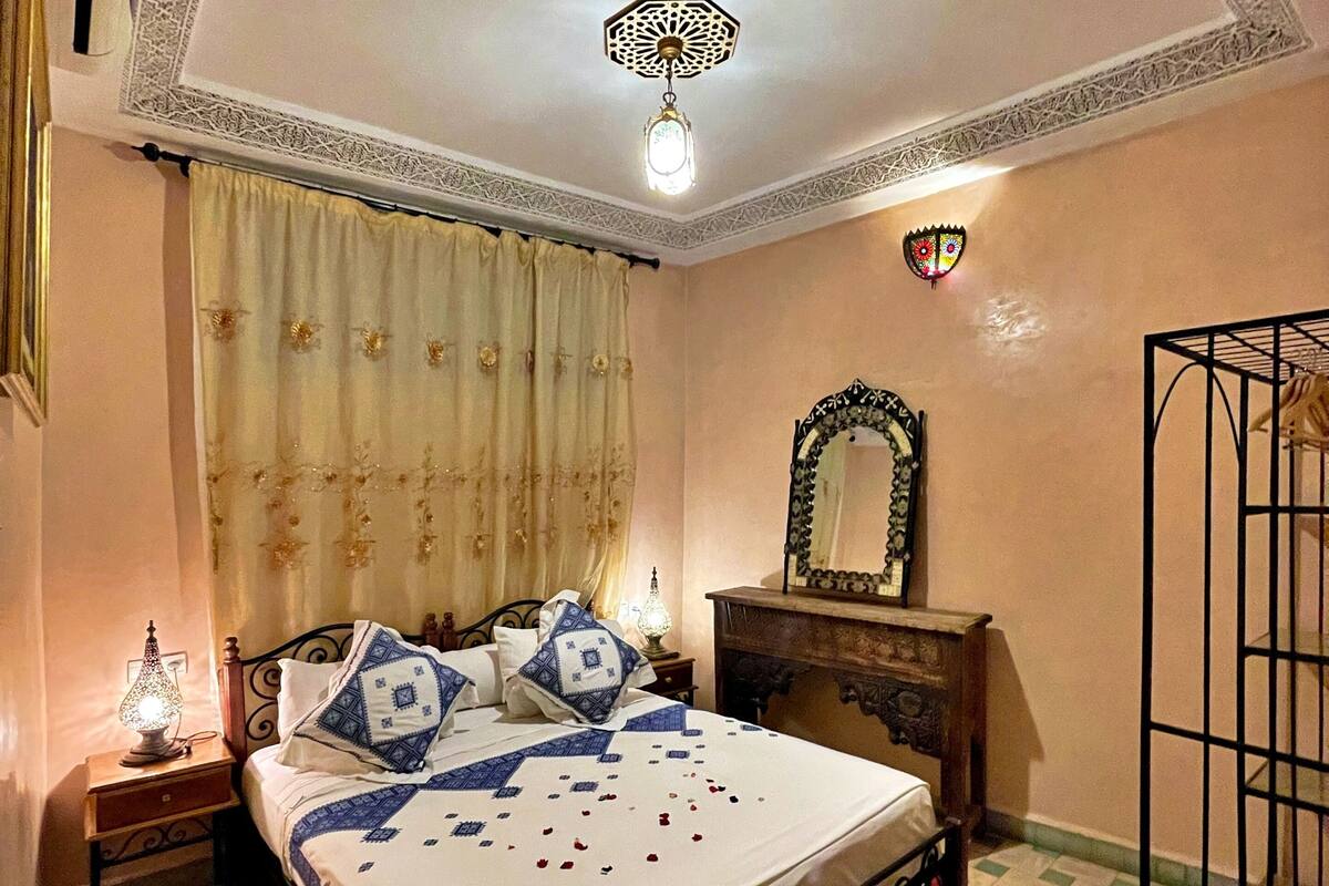 A bedroom with a bed, a nightstand, a lamp, a mirror, and a decorative ceiling light.