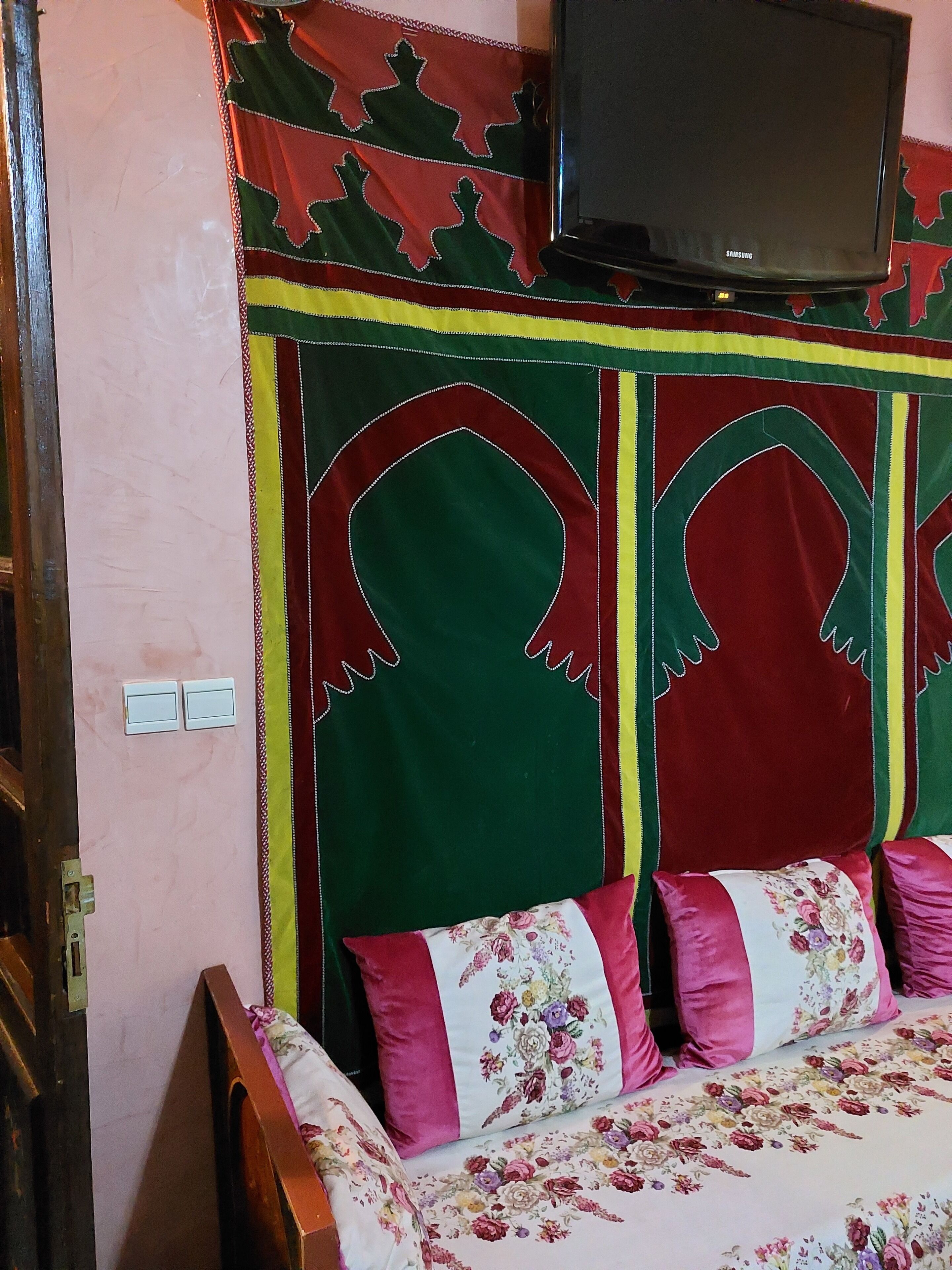 Un dormitori amb un llit, una televisió penjada a la paret i una pared decorada amb un dibuix.