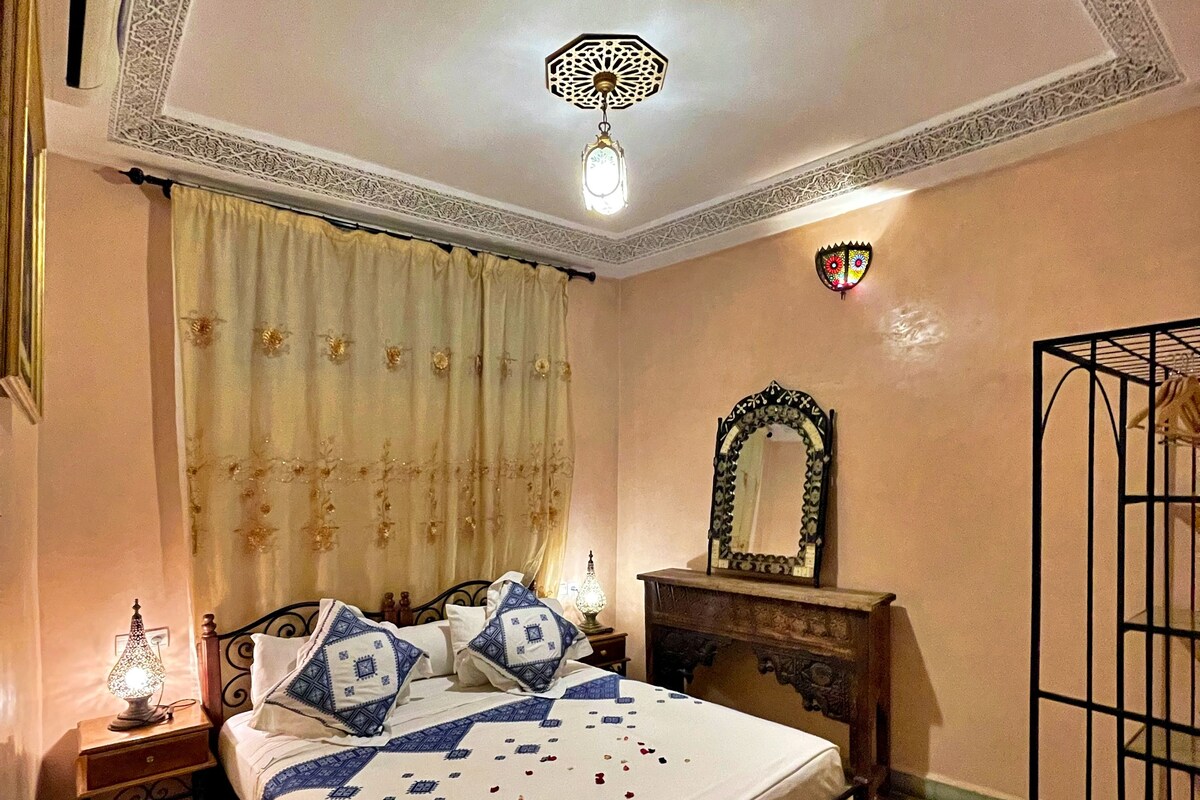 A bedroom with a bed, a nightstand, a lamp, a mirror, and a decorative ceiling light.