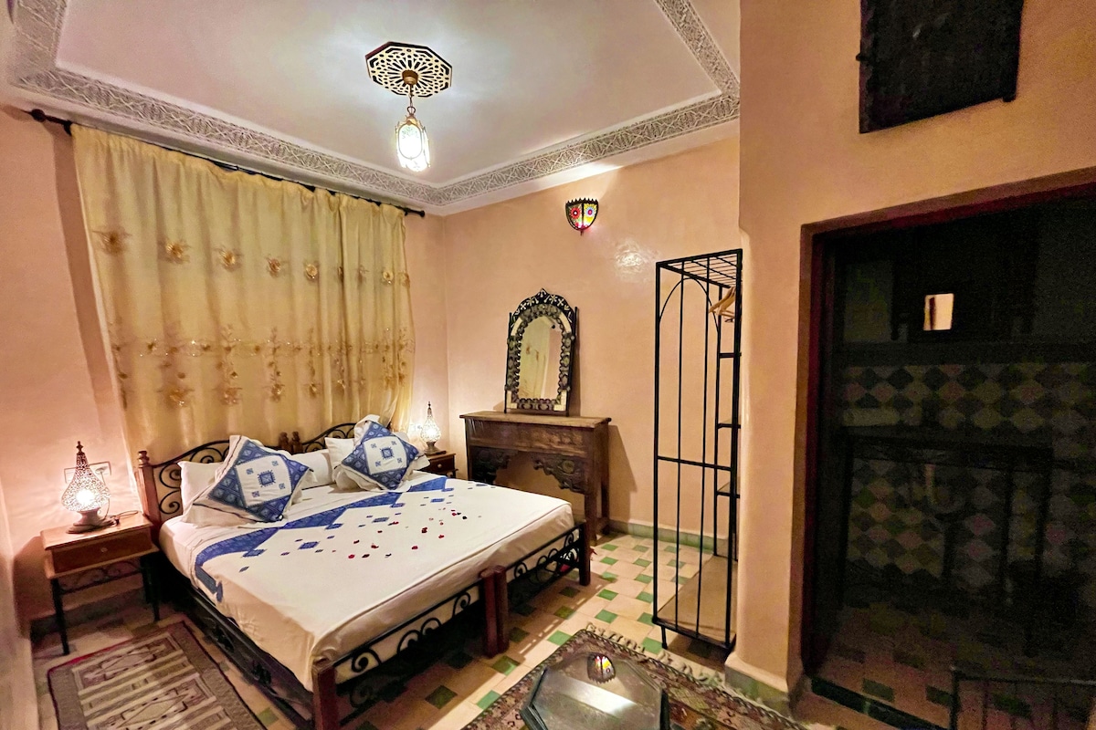 A bedroom with a bed, a nightstand, a mirror, a decorative wall piece, and a patterned floor.