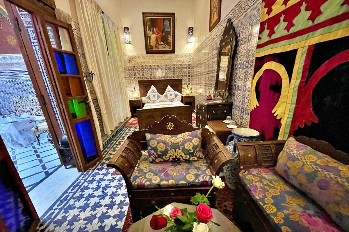 A traditional Moroccan room with a bed, sofa, and a small table with a vase of flowers.