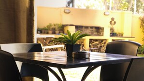 An outdoor dining area with a table and chairs, a potted plant, and a grill in the background. - A Sunflower Stop - Hostel (Cape Town)