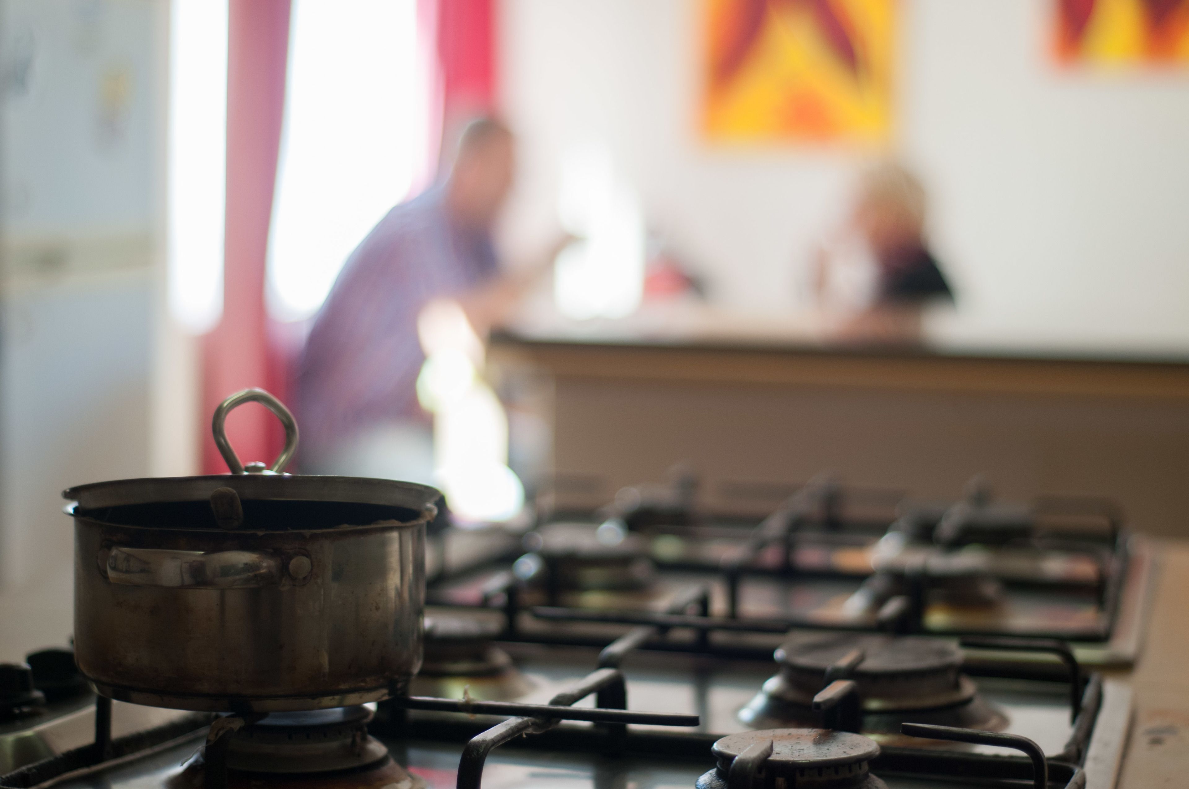 Una cocina con estufa a gas, una olla sobre la hornilla y un fondo desenfocado con una persona.