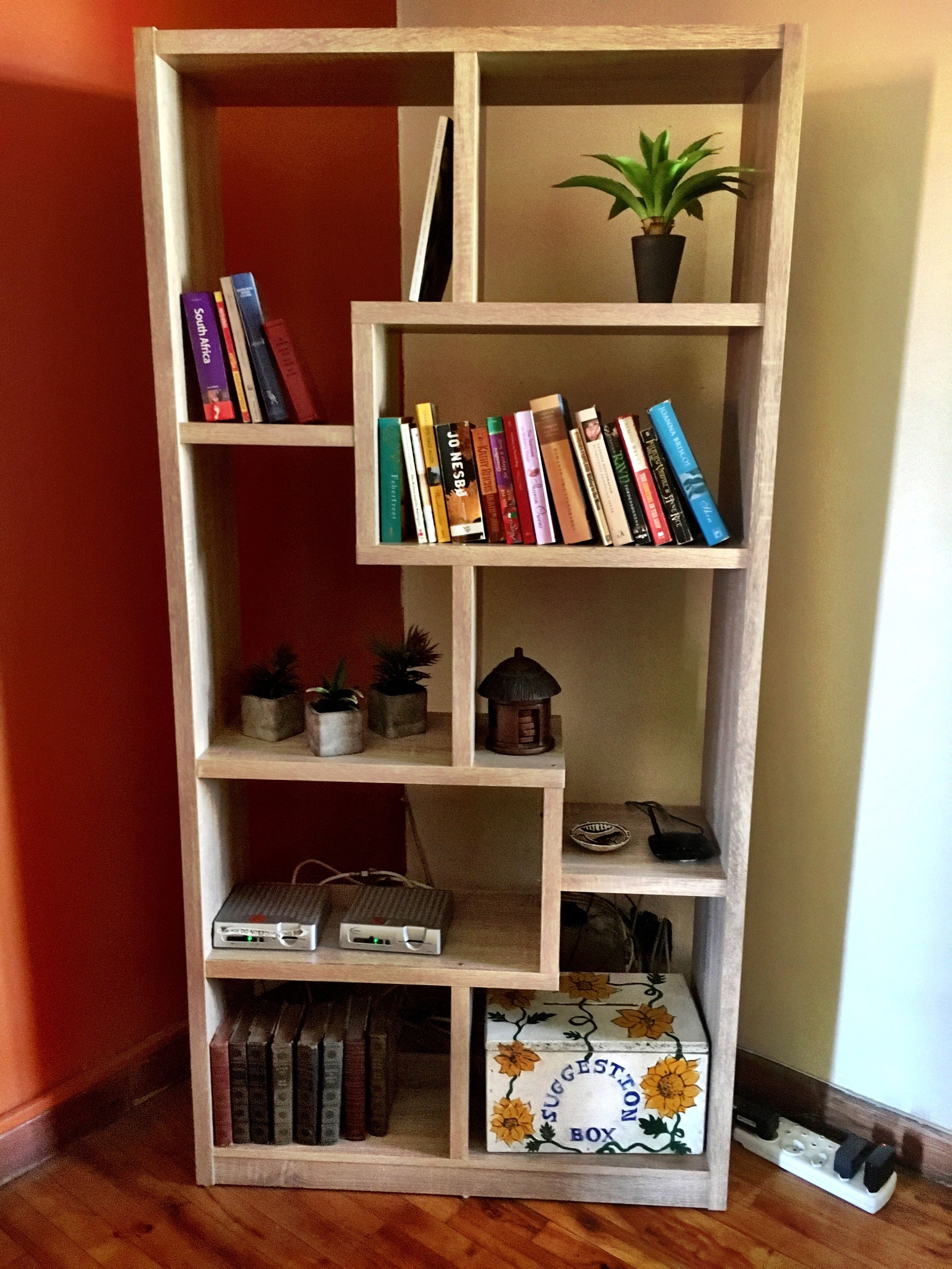 Ein hölzernes Bücherregal mit mehreren Ablagen, von denen einige mit Büchern und andere mit Dekorationen wie einer Topfpflanze und einer Laterne bestückt sind.