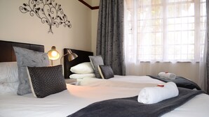A hotel room with a large bed, multiple pillows, a bedside lamp, and a window with curtains. - A Sunflower Stop - Hostel (Cape Town)