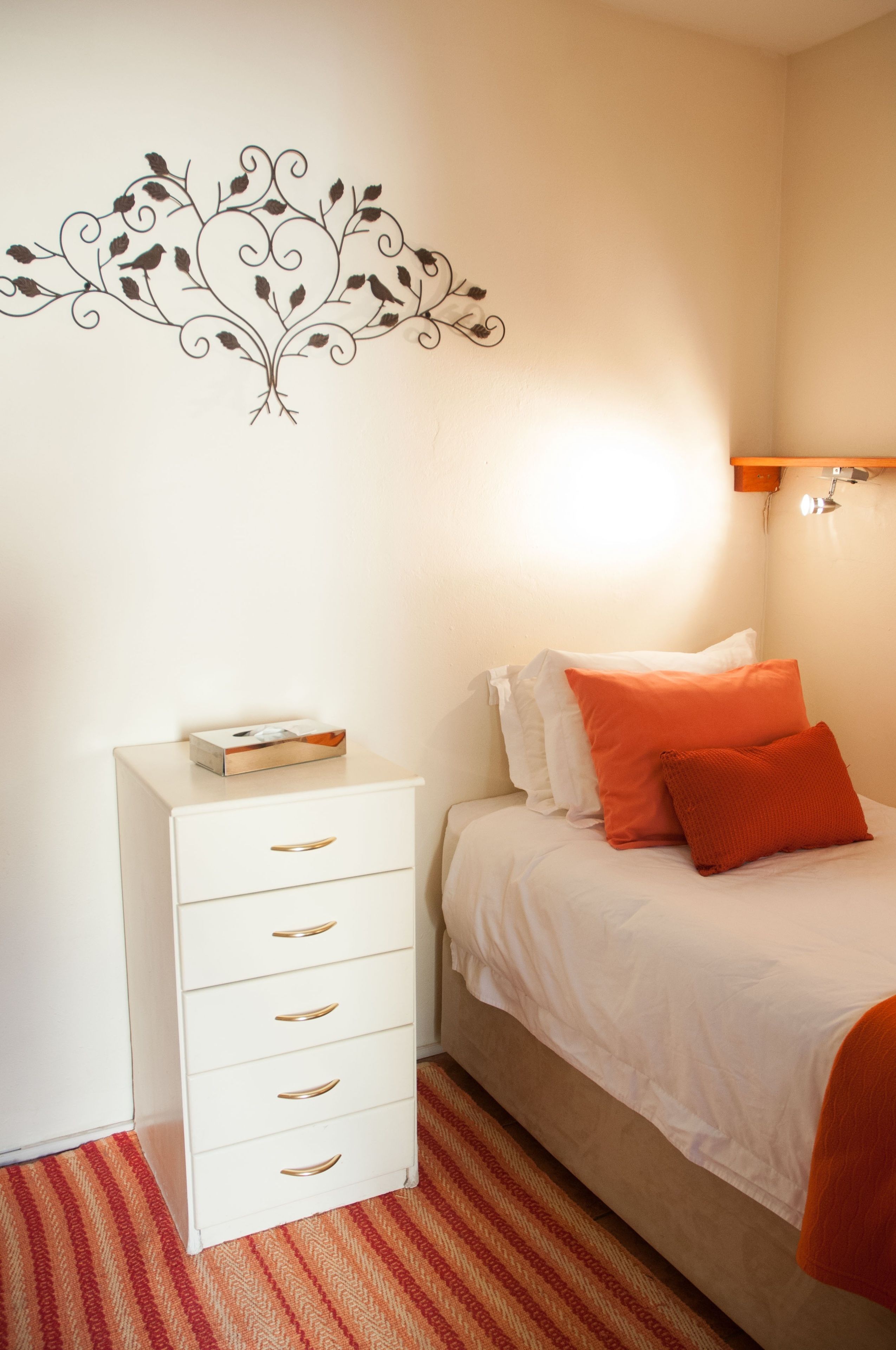 A bedroom with a bed, white nightstand, and a wall decoration.