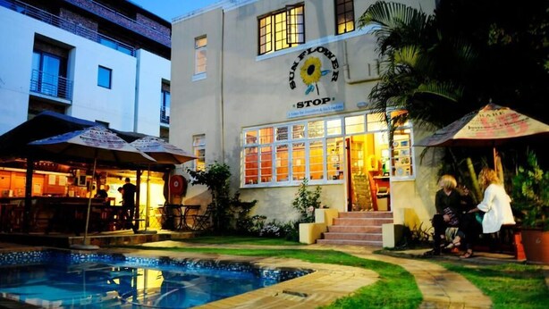 A building with a 'Sunflower Stop' sign, a pool, and outdoor seating areas. - A Sunflower Stop - Hostel (Cape Town)