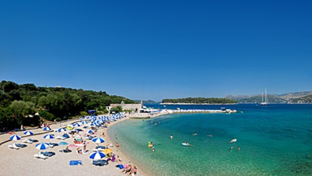 A beach with clear blue water, umbrellas, and people. - Anna Guesthouse (Dubrovnik)