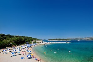 A beach with clear blue water, umbrellas, and people. - Anna Guesthouse (Dubrovnik)