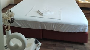 A neatly made bed with white linens, two bedside tables with lamps, a wall-mounted painting of flowers, and a vase with flowers on the left side. - Anna Guesthouse (Dubrovnik)