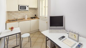 Cozinha compacta com micro-ondas, chaleira e um laptop sobre uma mesa.