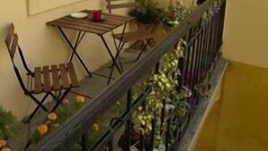 Uma varanda com mesa e cadeiras, uma janela e um corrimão com plantas em vasos.