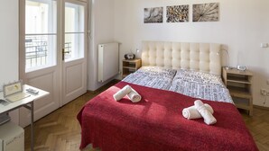 Quarto de hotel com uma cama grande, uma escrivaninha com um computador, um radiador e uma janela com vista para o exterior.