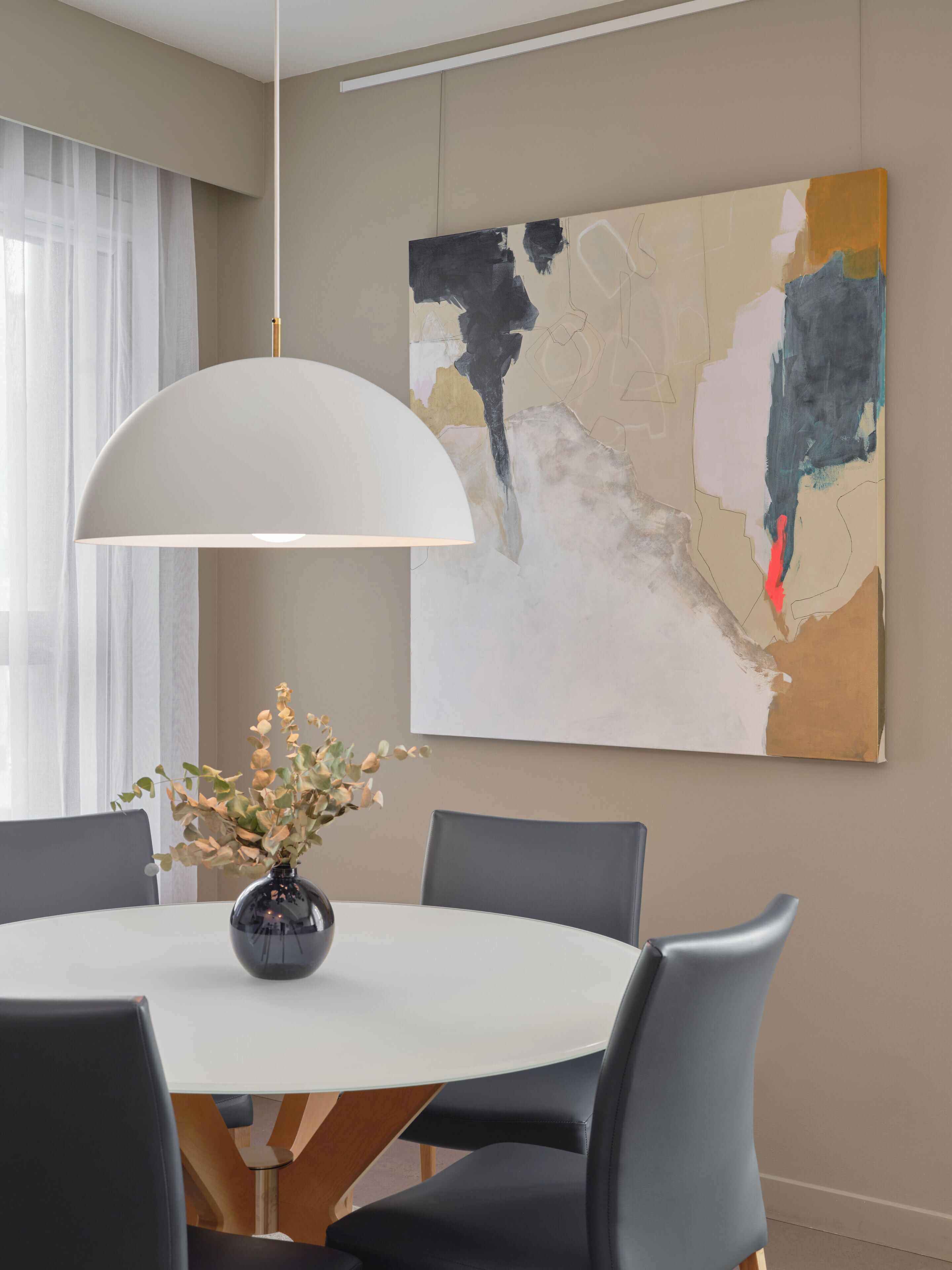 A modern dining area with a round table, six chairs, a white pendant light, and a large abstract painting on the wall.
