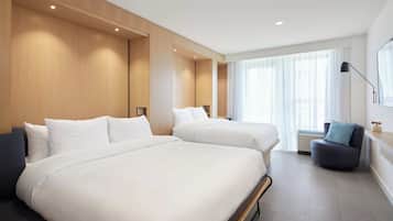 A modern hotel room with two beds, a seating area, and large windows.