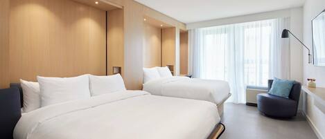 Una habitación de hotel moderna con dos camas, una zona de estar y ventanas amplias.