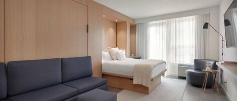 A modern hotel room with a sofa, a bed, a desk, and a chair.