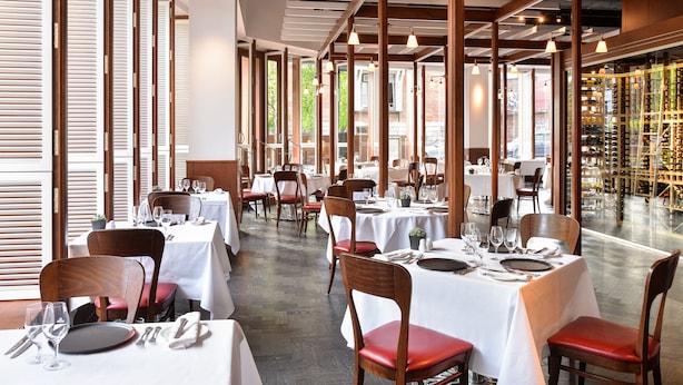 A restaurant with multiple tables set for dining, wooden chairs, and a wine rack in the background. - Hotel de l'ITHQ (Montreal)