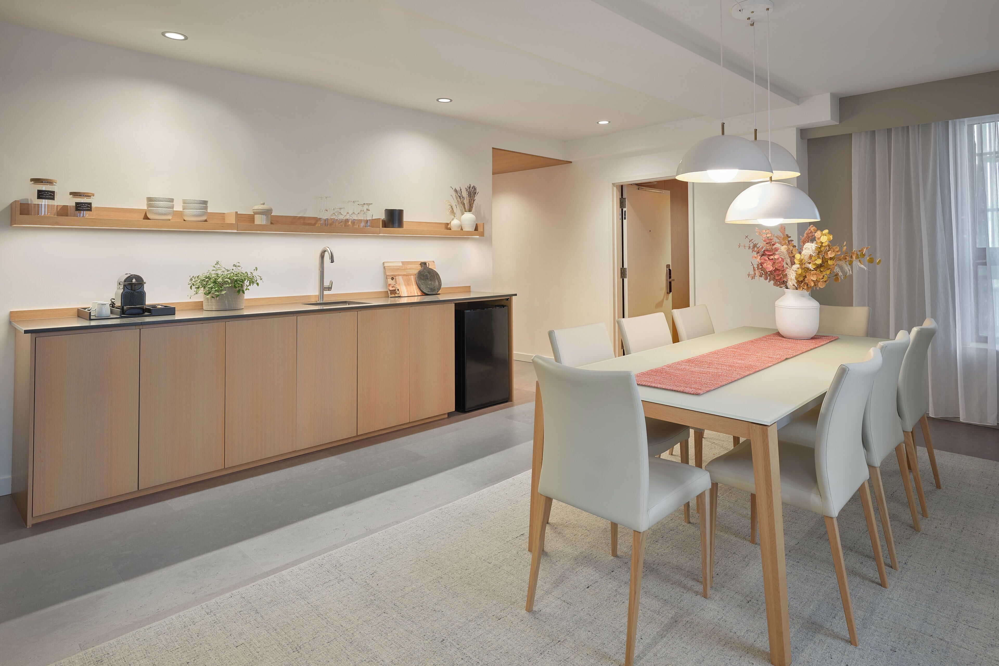 Une cuisine moderne avec des meubles en bois, un lave-vaisselle encastré et un coin repas comprenant une table et des chaises blanches.