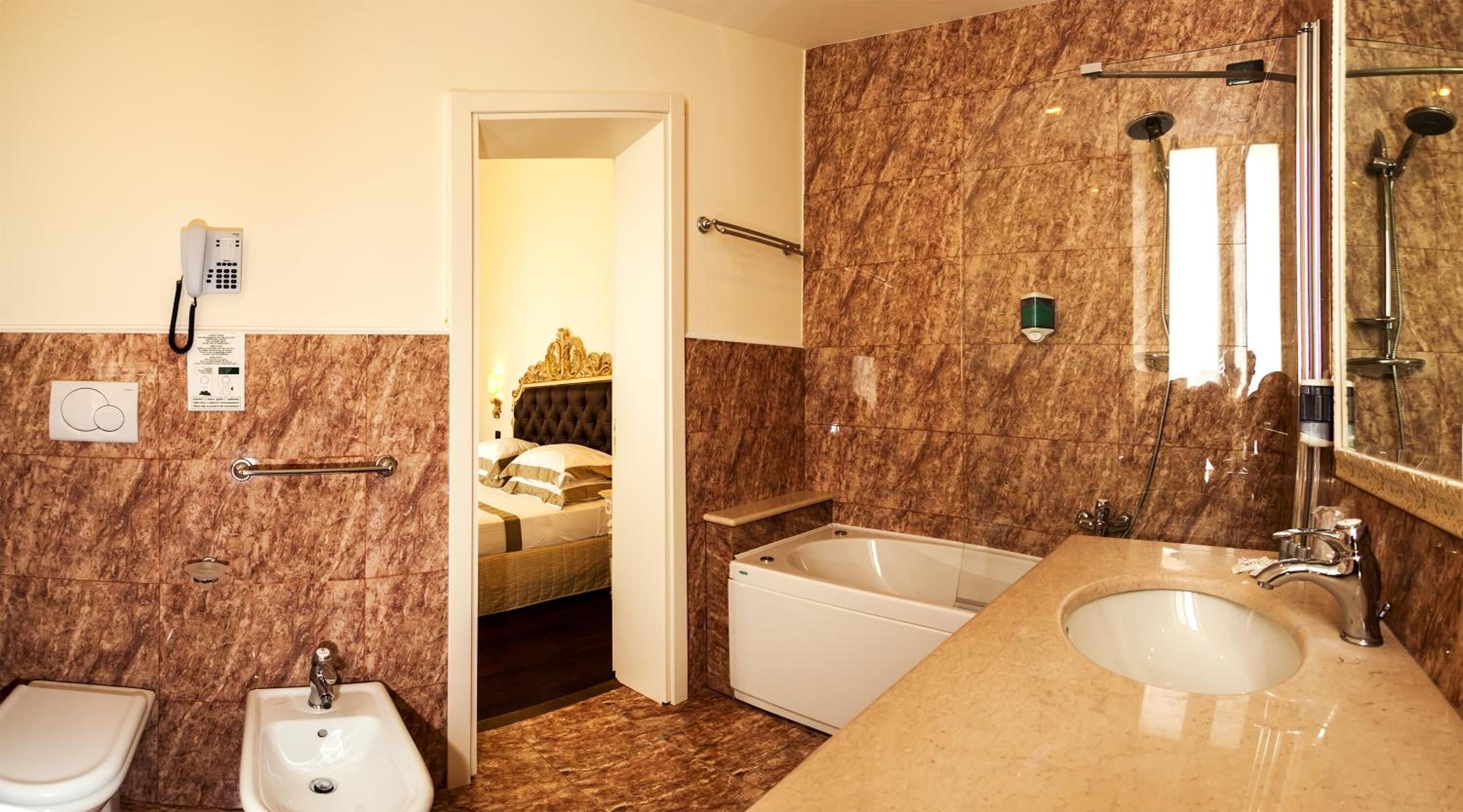 A bathroom with a bidet, a sink, a bathtub, and a shower. There is a door leading to a bedroom with a bed and a nightstand.
