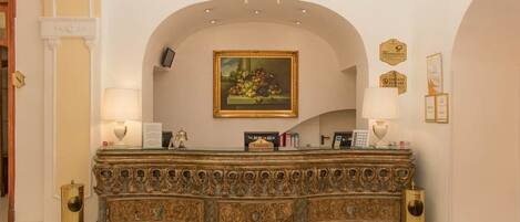 A reception area with an ornate desk, a chandelier, framed artwork, and a clock on the wall.
