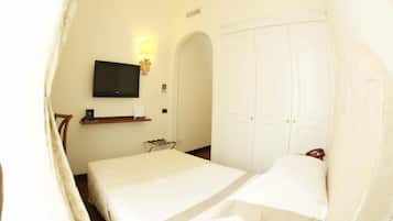 Habitación de hotel con cama, televisor montado en la pared, armario y una pequeña mesa con lámpara.