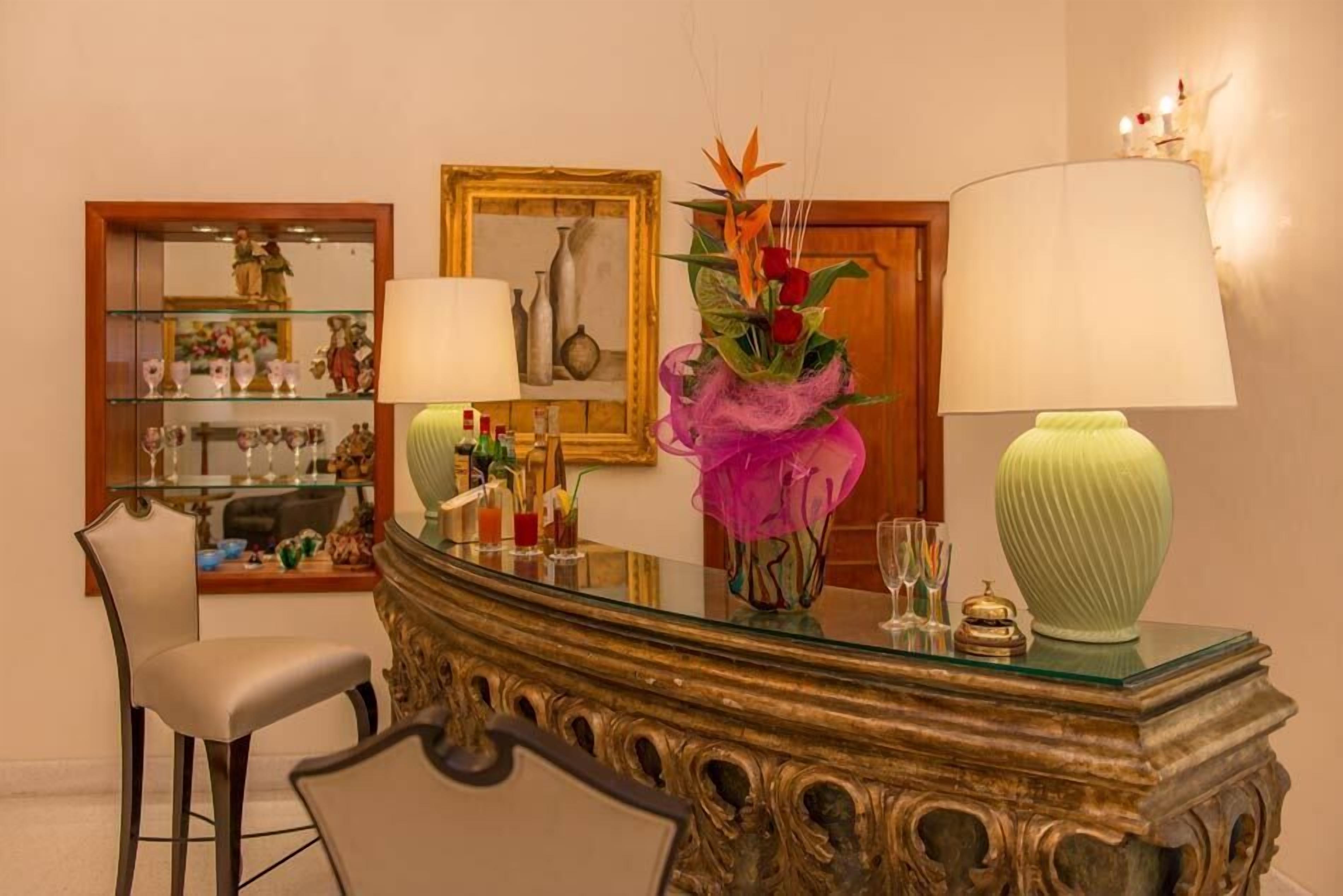 Ein gut beleuchteter Raum mit Schreibtisch mit Glasplatte, einem Stuhl, einem Spiegel und einer Vase mit Blumen.