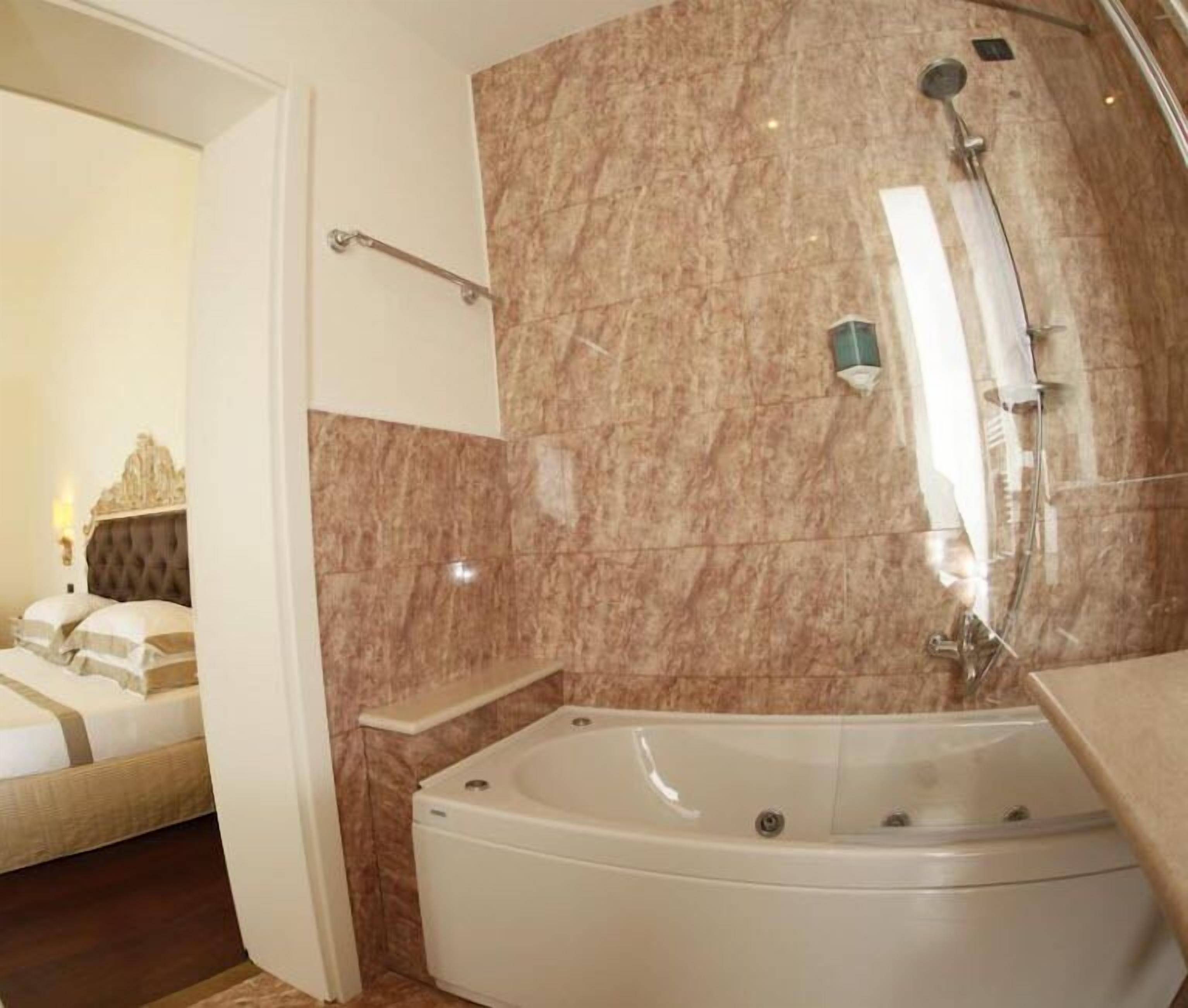 A modern bathroom with a large bathtub, marble walls, and a visible shower area.