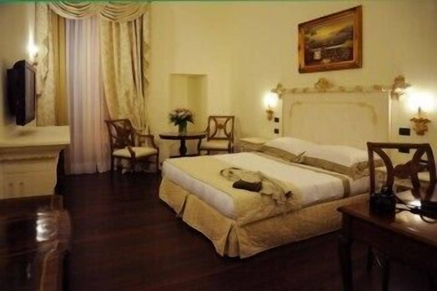 A hotel room with a large bed, two chairs, a small table, and a painting on the wall.