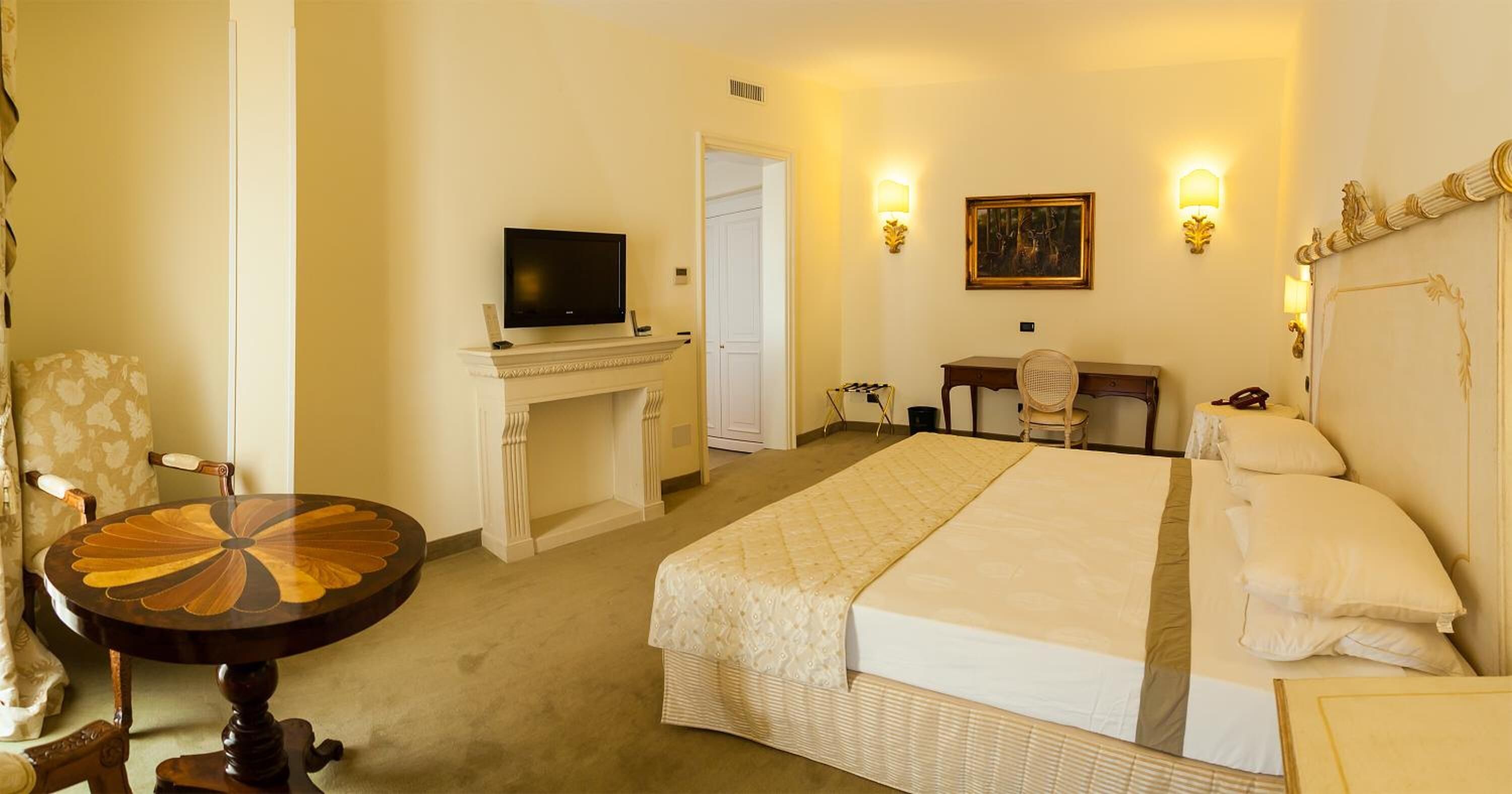 A hotel room with a large bed, a desk with a television, a chair, and two wall-mounted lamps.