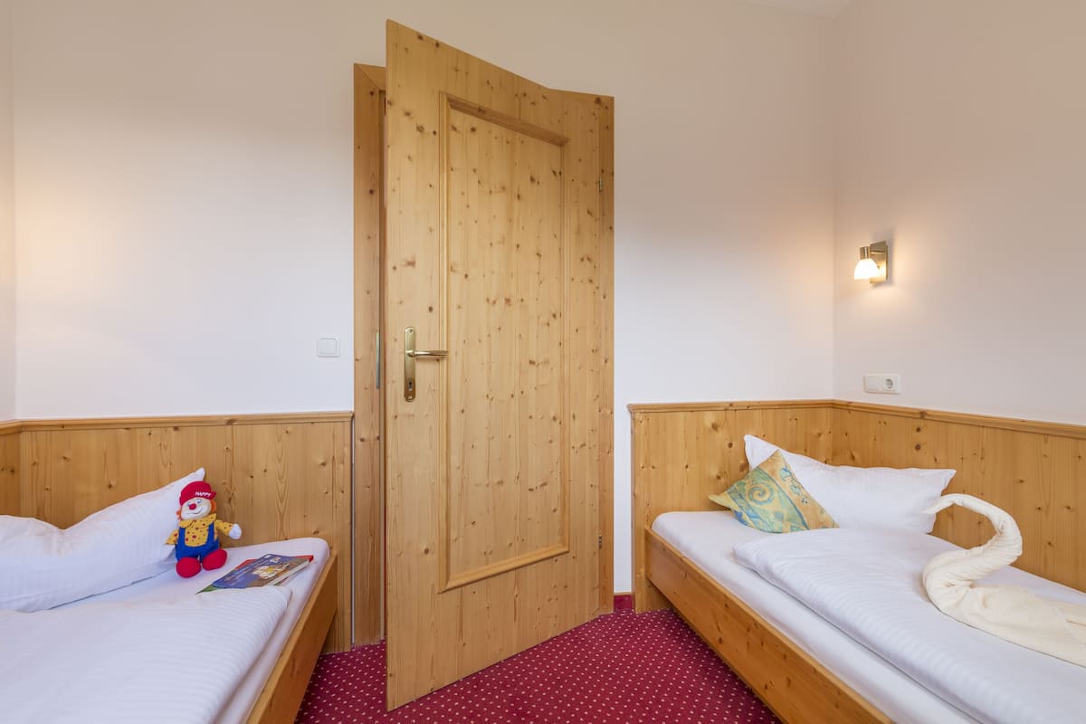 A room with two wooden beds, a wooden door, and a small wall-mounted light fixture.