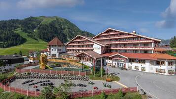A large hotel with multiple balconies, a playground, and a parking area with various vehicles.