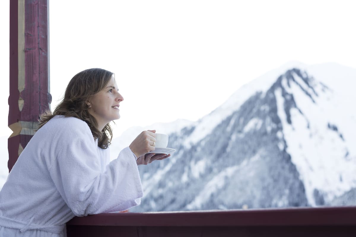 A person in a white robe holding a cup, overlooking a snow-covered mountain.