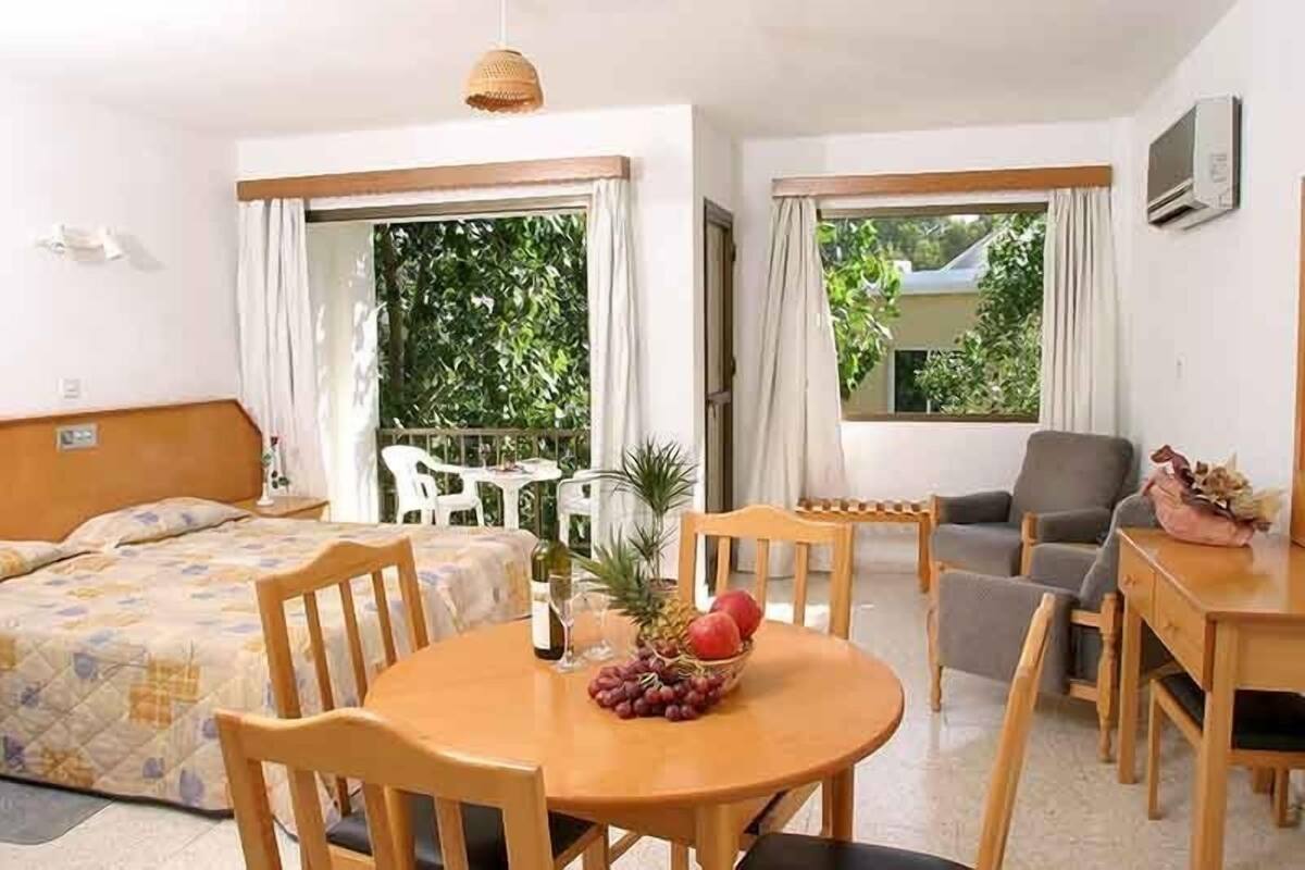 Quarto de hotel com cama, mesa de jantar e cadeiras, um pequeno sofá e uma janela com cortinas.