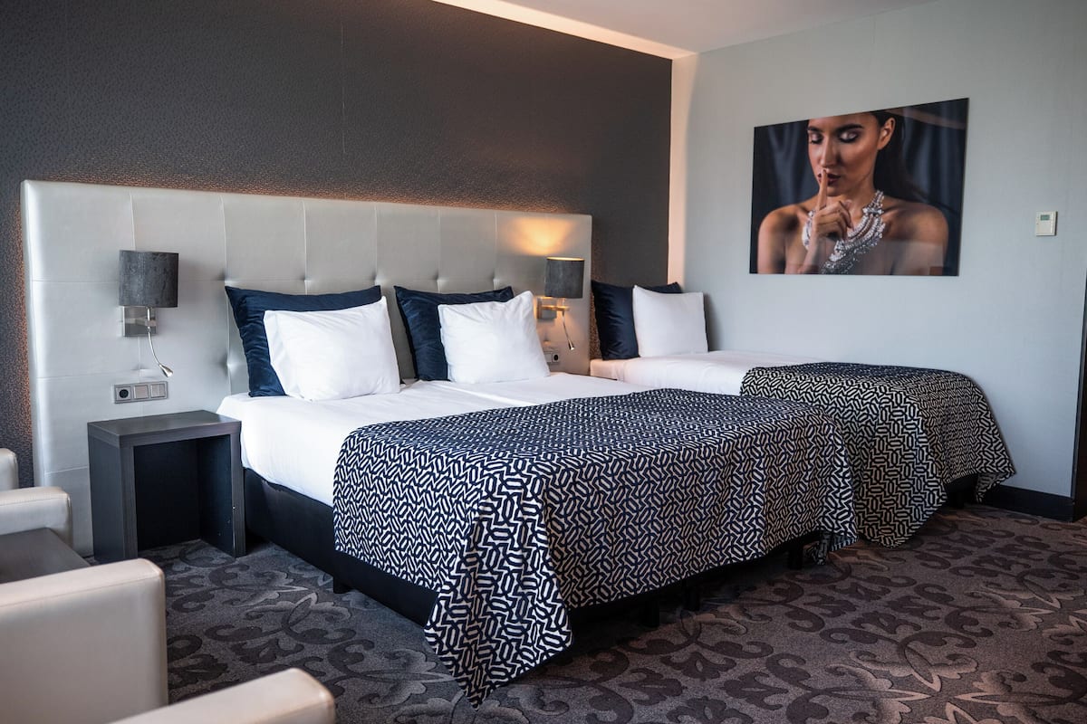 A hotel room with two beds, a headboard, bedside tables, a wall-mounted picture, and a patterned carpet.