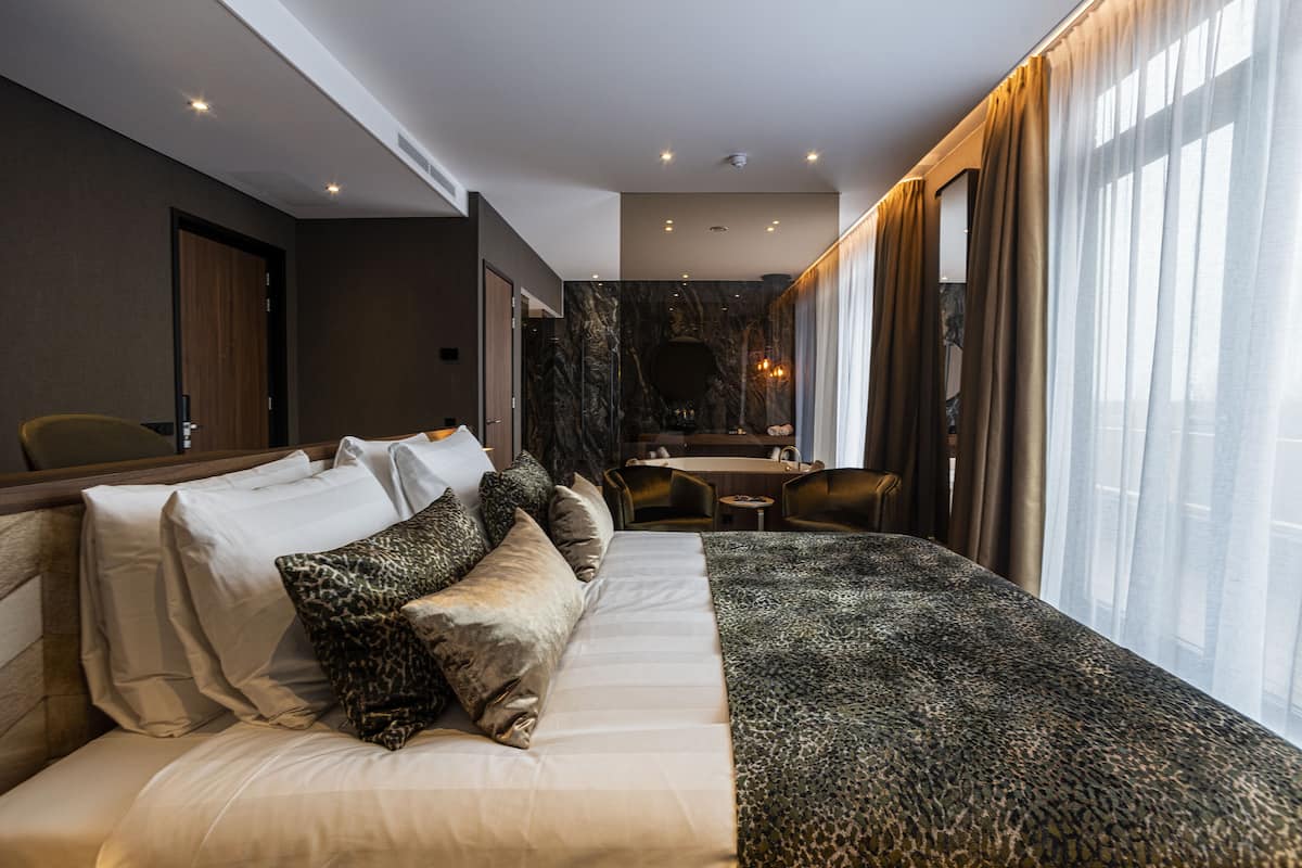 A modern hotel room with a large bed, a dining area, and a view of the city.