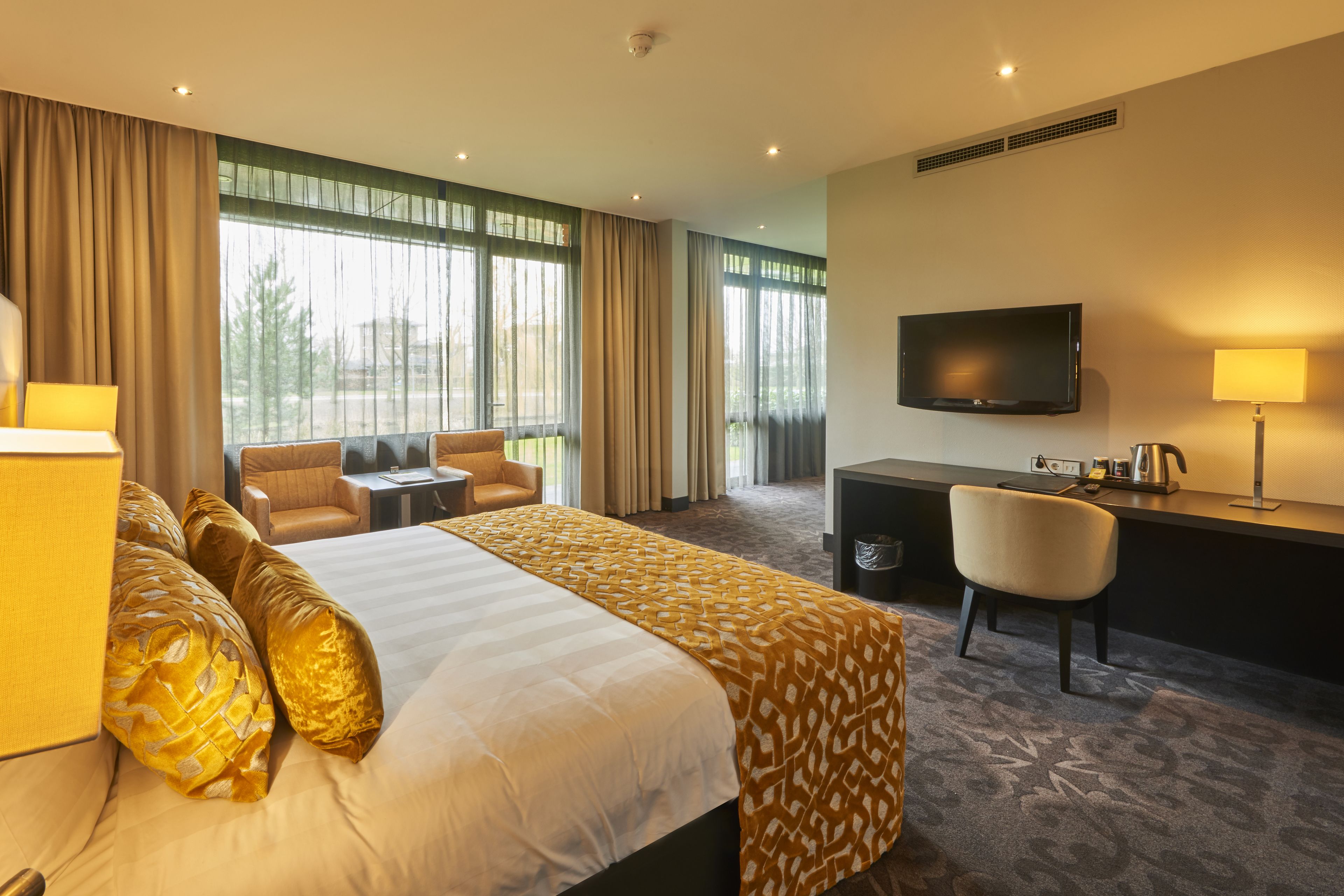 A hotel room with a large bed, a desk, a chair, a television, and a window with curtains.