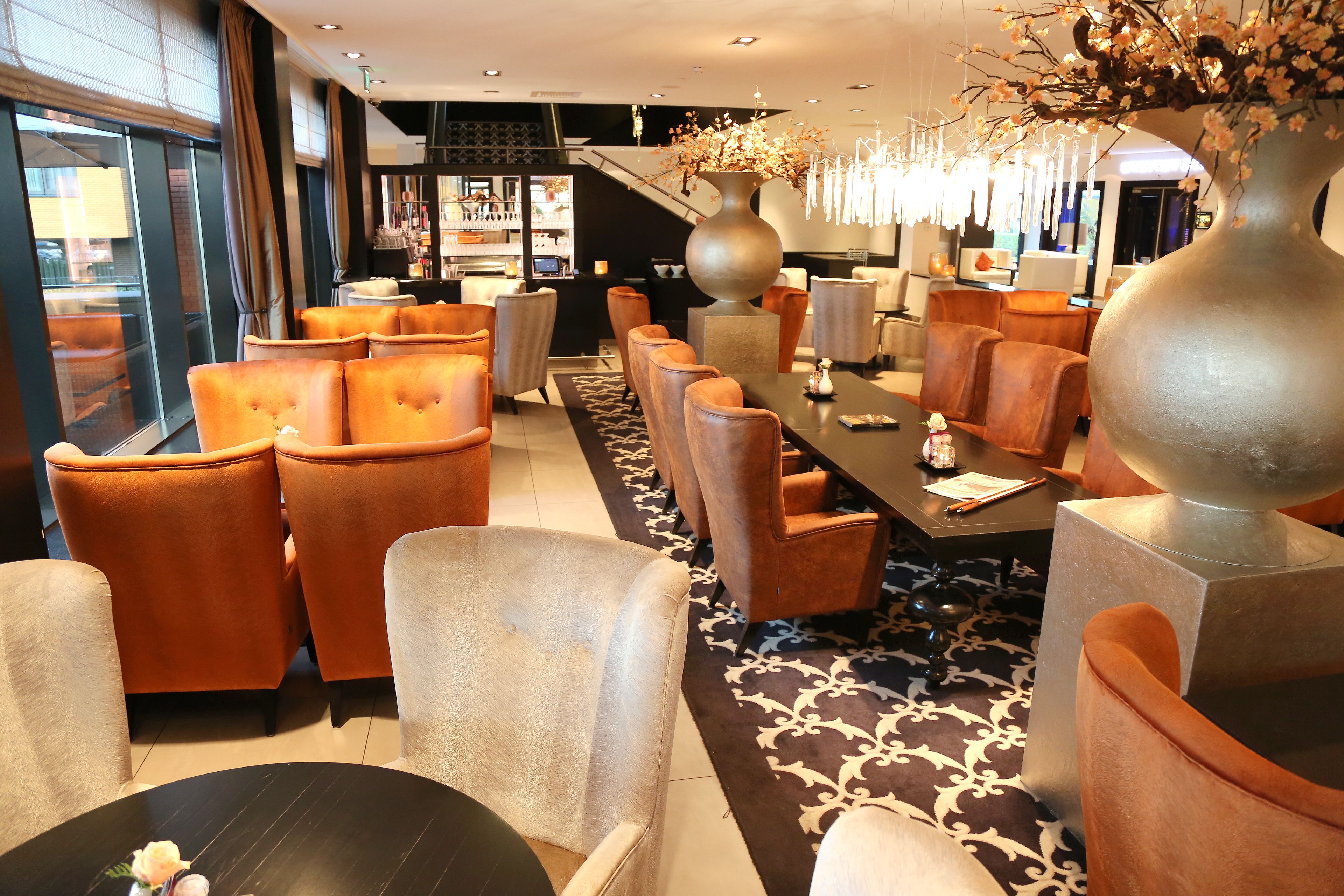 A modern hotel lobby with leather seating, a large vase with flowers, and a staircase in the background.