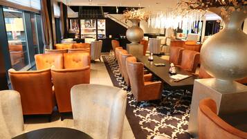 A modern hotel lobby with leather seating, a large vase with flowers, and a staircase in the background.