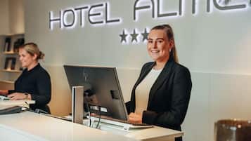 Een receptiebalie met een computer en telefoon, en een muur met de tekst 'HOTEL ALME' en drie sterren.