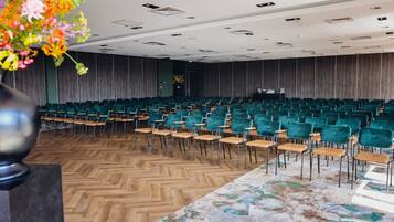 A conference room with rows of teal chairs and a wooden floor, a marble table, and a floral arrangement.