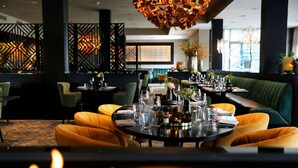 Un restaurant avec des tables rondes, des banquettes recouvertes d’un tissu vert et un luminaire décoratif au plafond.