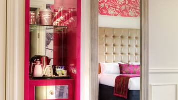 A hotel room with a pink minibar, a tufted headboard, and a floral-patterned wall.