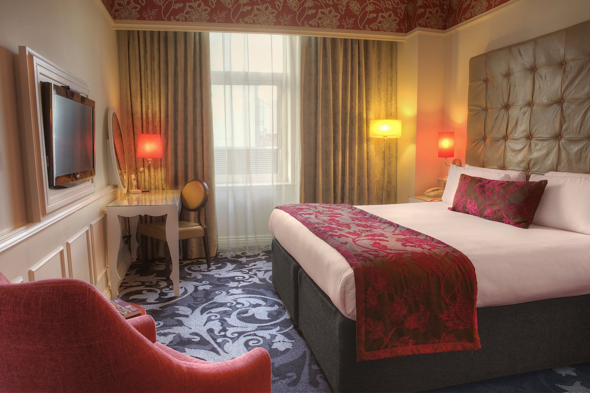 A hotel room with a bed, a desk, a chair, a television, and two lamps.