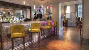 Zona de bar con una barra de mármol, varios taburetes y una gran variedad de botellas.