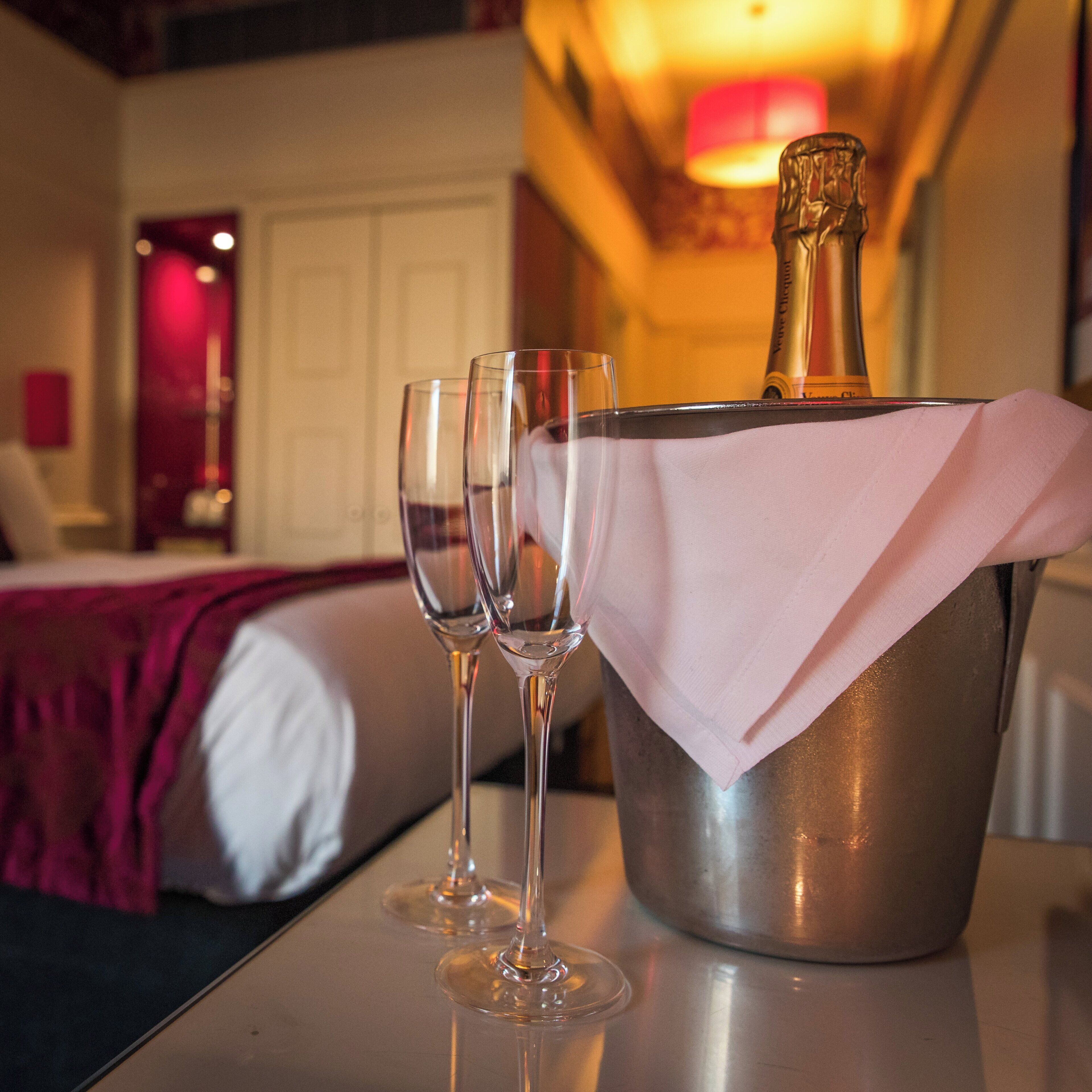 Une chambre d’hôtel avec un lit, une table de chevet et une bouteille de champagne dans un seau à glace.